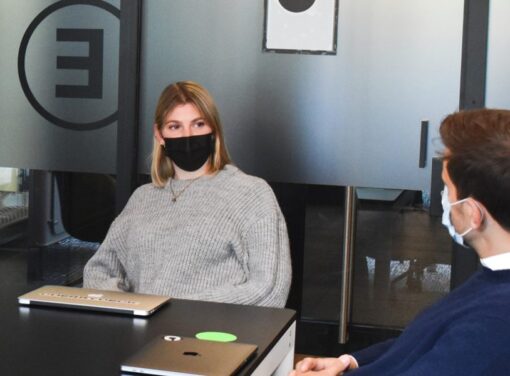 Female business professional sitting at desk in meeting room with COVID mask on having conversation with colleague