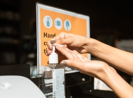 Hands reaching in to pump hand sanitizer in front of COVID safety sign