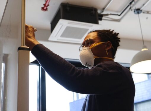 Business person in office with COVID mask on writing on white board