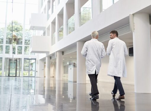 Two male physicians walking down hospital atrium and talking