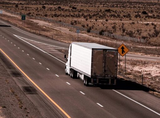 View of back of tractor trailer driving down highway on a summer day