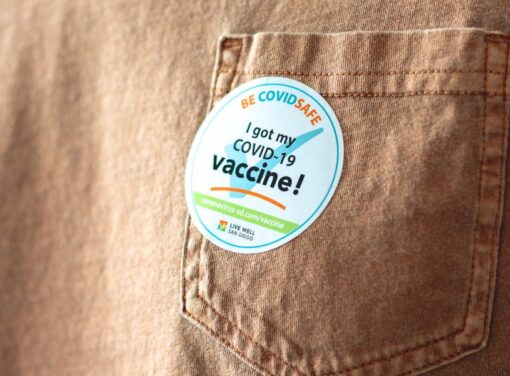 Close up photo of someone's pale orange t shirt with sticker that reads "I received my COVID-19 vaccination shot"