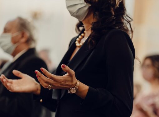 Funeral service attendee holding up hands in prayer with COVID face mask on