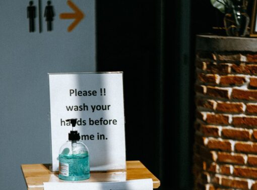 Table out front of business with sign that reads "please sanitize before you come in" with a bottle of hand sanitizer next to it