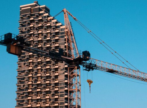 close up photo of construction crane in front of large skyscraper building frame