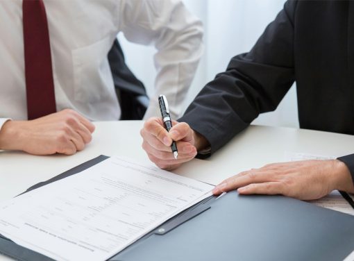 Man with pen signing paper at desk with boss