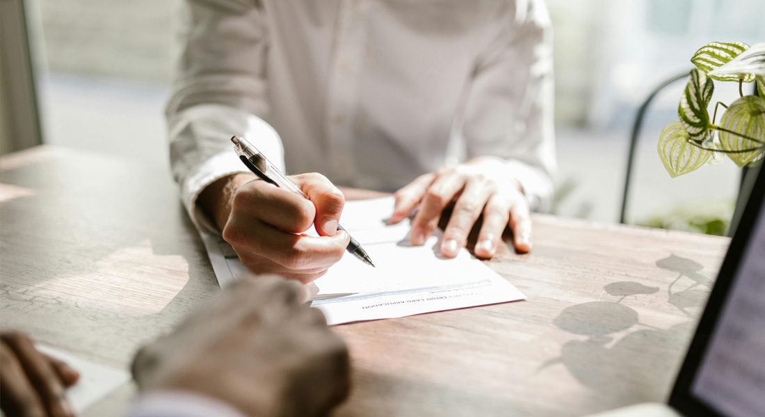 person signing paper at desk in front of boss