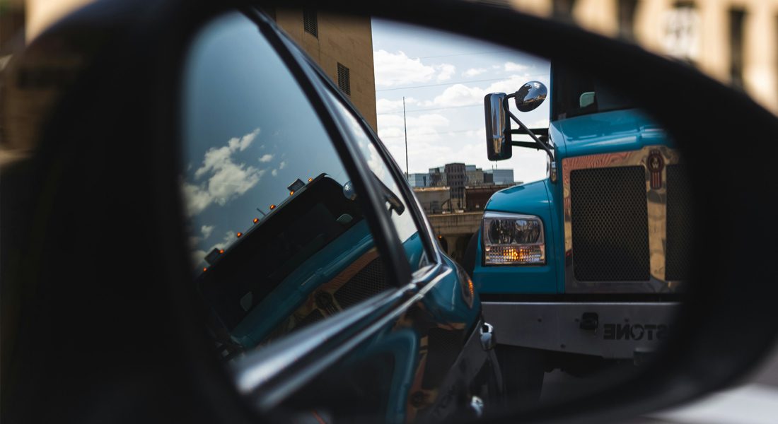 Rear-view mirror of car with close up of semi-truck in sight